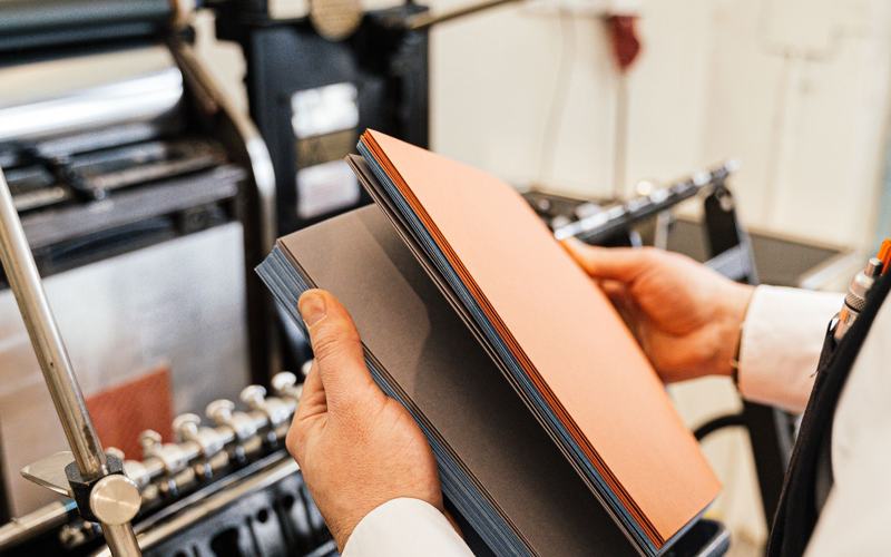 Baskıdan yeni çıkmış turuncu kapaklı katalog formalarını inceleyen eller